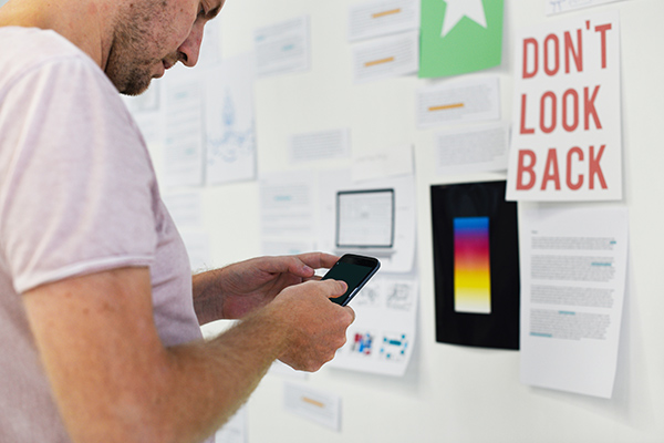 Young man looking at his phone in front of bulletin board